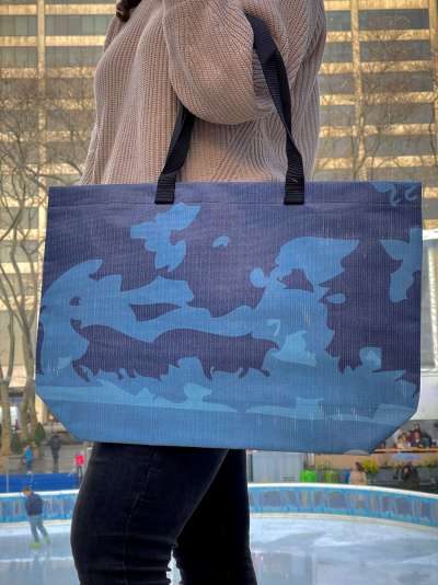 A woman carries a Winter Village barricade tote made from fabric that once covered barricades in Bryant Park New York City.