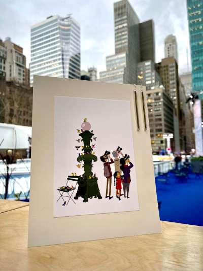 A print of Bryant Park NYC and a pair of lawn earrings sit on a counter with the skating rink in the background.