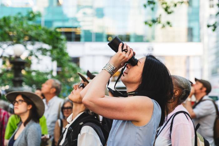 Woman with binoculars spies a bird in Bryant Park NYC during the park's birding tour.