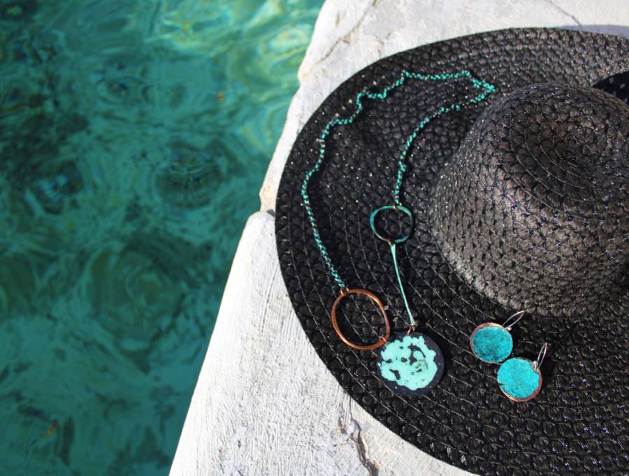 A necklace is draped over a summer hat next to the water.