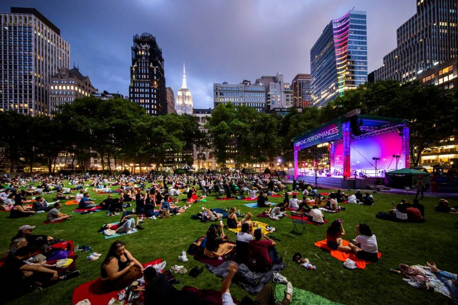 People sit on the lawn in Bryant Park with bands on the stage for Bryant Park's Emerging Music Festival.