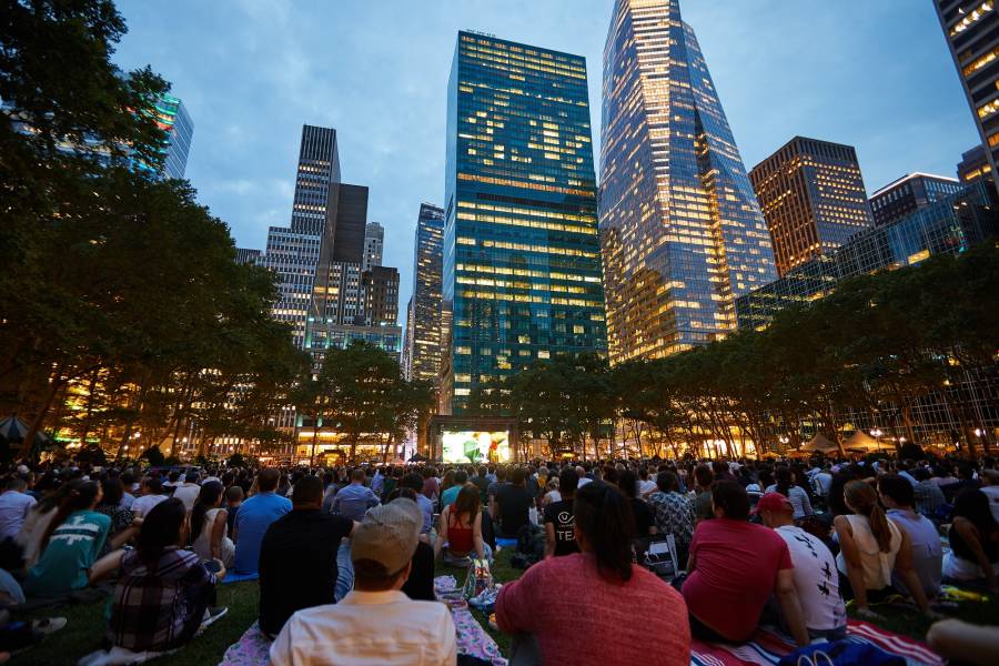 Tons of people sitting on the lawn at night watching a feature film in Bryant Park NYC, as part of their summer movie nights.