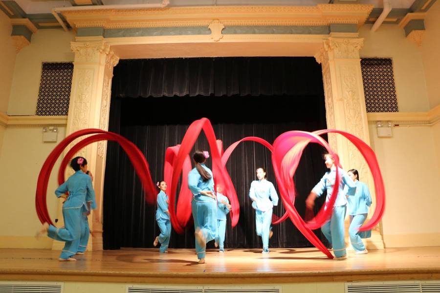 Dancers perform on stage with large red ribbons.